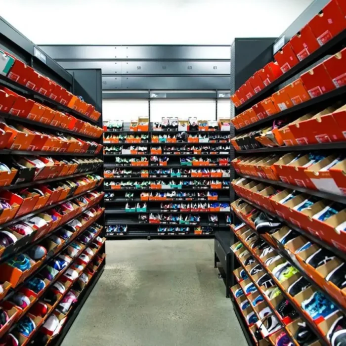 Couloir d'un entrepôt de sneakers avec des centaines de boîtes Nike empilées sur des étagères noires, typique du stock d'un revendeur professionnel sur Whatnot