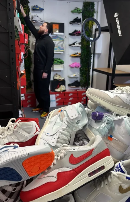 Vendeur Whatnot en train de préparer son live sneakers avec un ring light professionnel, un mur de boîtes Nike et Jordan en fond et des paires Air Max et Off-White au premier plan