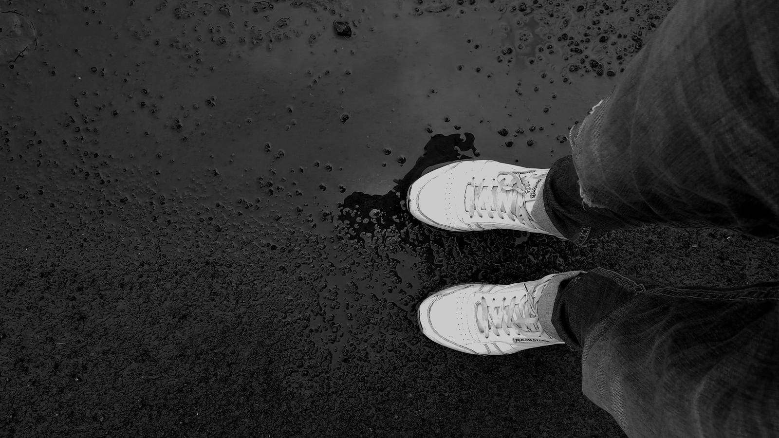 Sneakers blanches sur un bitume mouillé, vues du dessus en noir et blanc