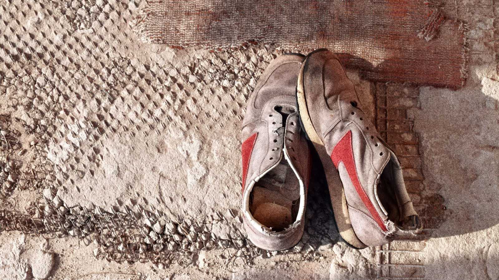 Paire de sneakers très usées abandonnées contre un mur de briques