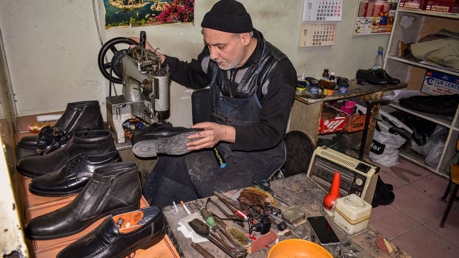 Cordonnier à sa machine, chaussures alignées sur l'établi