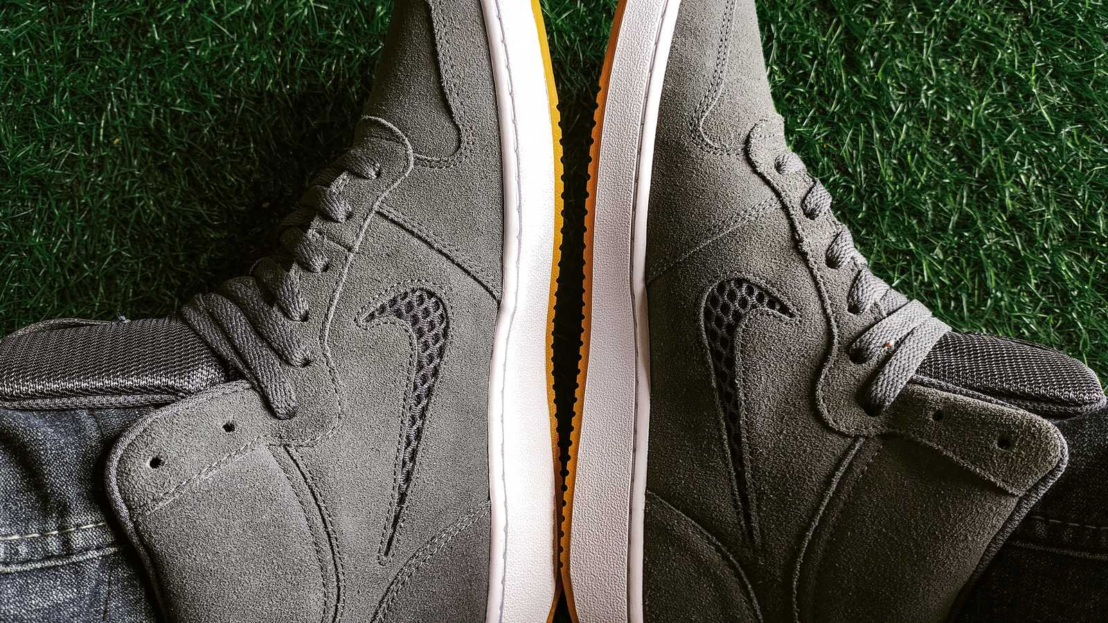 Gros plan sur deux sneakers montantes en daim gris posées sur de l'herbe