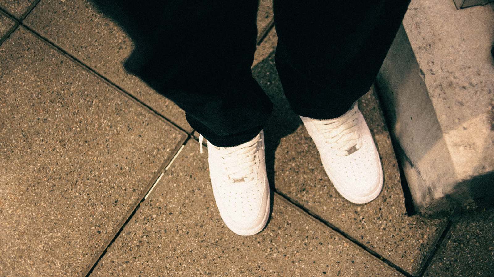 Sneakers blanches portées avec un pantalon noir sur un dallage