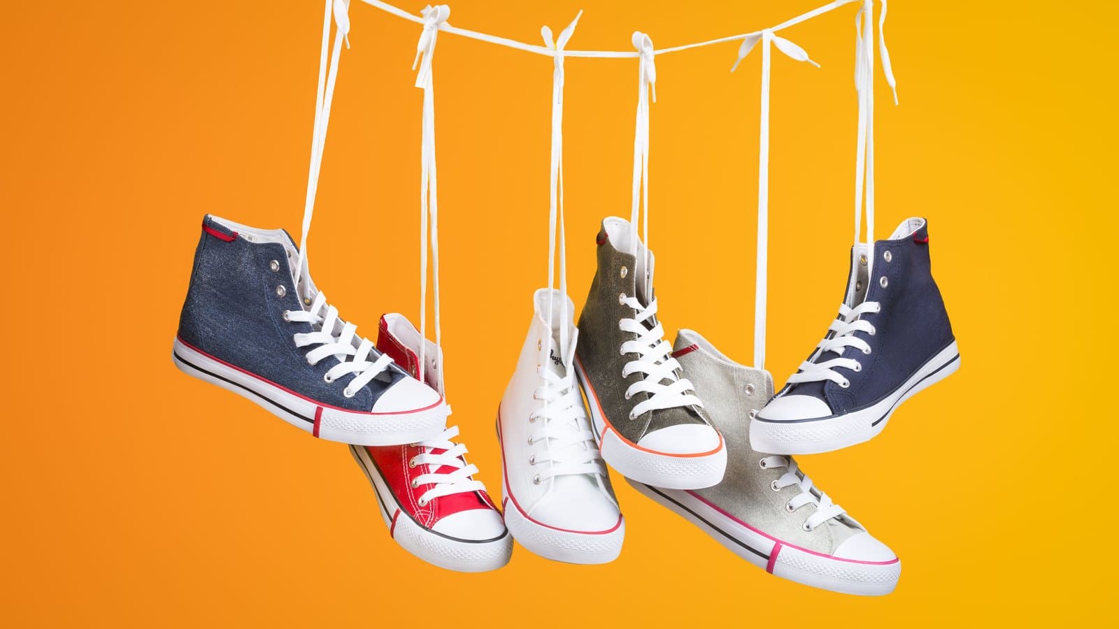 Quatre paires de sneakers en toile suspendues par leurs lacets sur fond orange