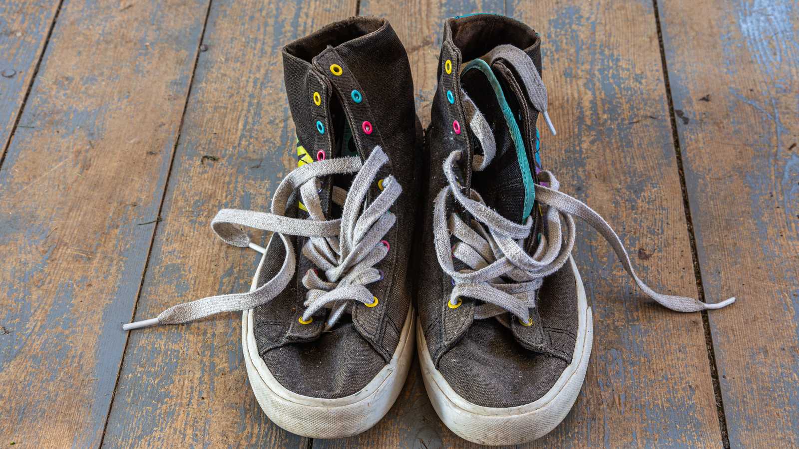 Sneakers montantes usées à lacets blancs posées sur un plancher