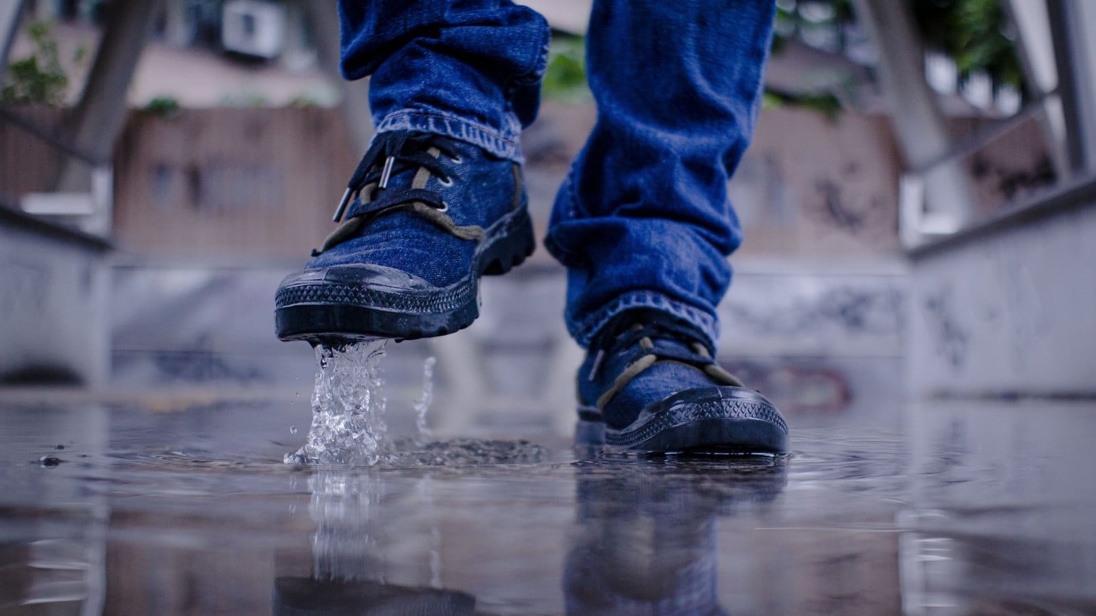 Sneakers bleues éclaboussant une flaque d'eau sur un sol mouillé