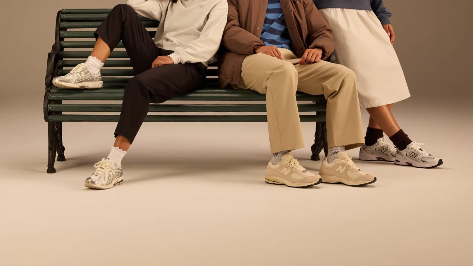 Trois paires de sneakers New Balance argentées et beiges, portées sur un banc